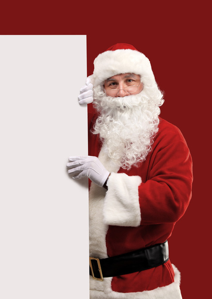 Happy Santa Claus looking out from behind the blank sign isolated on red background with copy space - Photo, Image