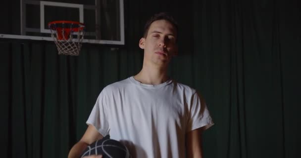 Popular Caucasian basketball player portrait playing with a basket ball on a background serious confident look white T-shirt - Záběry, video