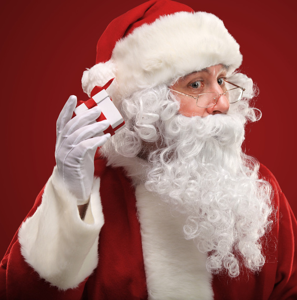 Photo of Santa Claus holding red giftbox by his ear - 写真・画像