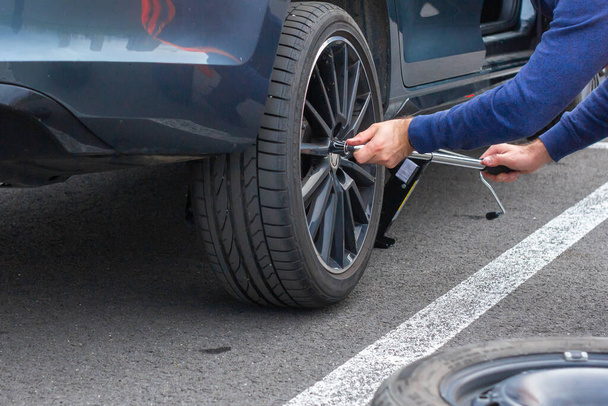 Close up mans hands changing a wheel usinf srewdriver. Replacing winter and summer tires. Seasonal tire replacement concept. Service process. Prague, March, 2020 - Foto, imagen
