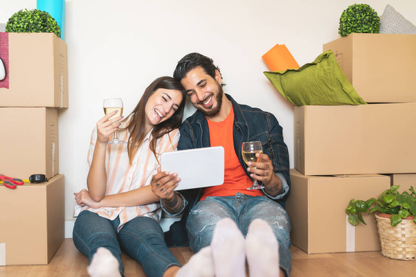 Ευτυχισμένο νεαρό ζευγάρι κινείται σε νέο σπίτι ακινήτων - Νέοι εραστές διασκεδάζουν χρησιμοποιώντας tablet online ψώνια κάθεται δίπλα κουτί χαρτοκιβώτιο - Αλλαγή διαμέρισμα ημέρα και τους ανθρώπους έννοια σχέση ζωής - Φωτογραφία, εικόνα