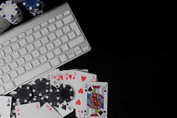 Cards and poker chips next to isolated computer keyboard on black background. Betting and online game concept. With copy space - Photo, Image
