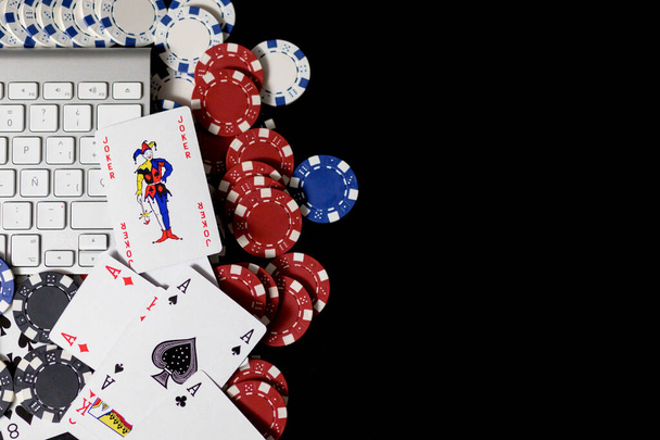 Pôquer fichas vermelhas, azuis e brancas e cartões em torno de um quadro de chaves do computador isolado em fundo preto.Aposta e conceito de jogo online.Copiar espaço
 - Foto, Imagem