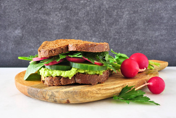 Gesundes grünes Sandwich mit Avocado, Gurke, Spinat und Rettich. Seitenansicht auf Servierbrett. - Foto, Bild