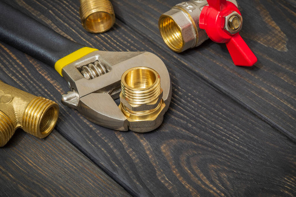 Encanamento acessórios de latão e chave ajustável closeup em um placas de madeira preta durante a reparação ou substituição de peças de reposição
 - Foto, Imagem