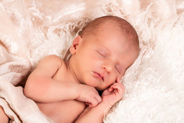 Ein kleiner Junge schläft friedlich bei seinem ersten professionellen Fotoshooting. Er ist weiß gekleidet und mit einer weißen Decke bedeckt. - Foto, Bild