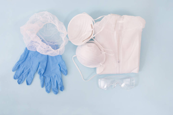 Staubmaske, blaue Handschuhe, Schutzanzug und Kopfbedeckung isoliert auf hellblauem Hintergrund. - Foto, Bild