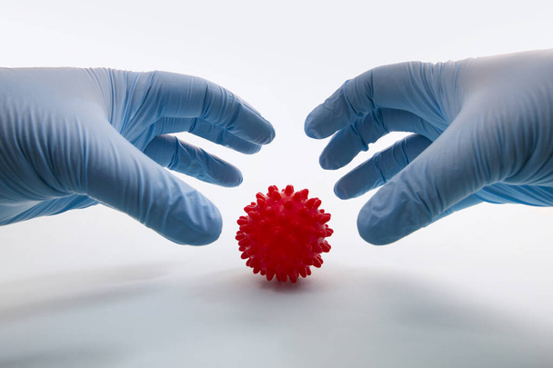 Doctor's hand holding red virus ball concept over a light blue background. - Zdjęcie, obraz