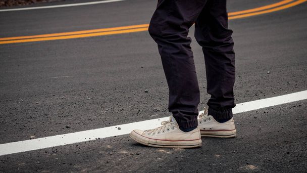 Мужчины носили кроссовки стоя на асфальтированных дорогах с желтыми и белыми полосами движения, пересекающими горы
. - Фото, изображение