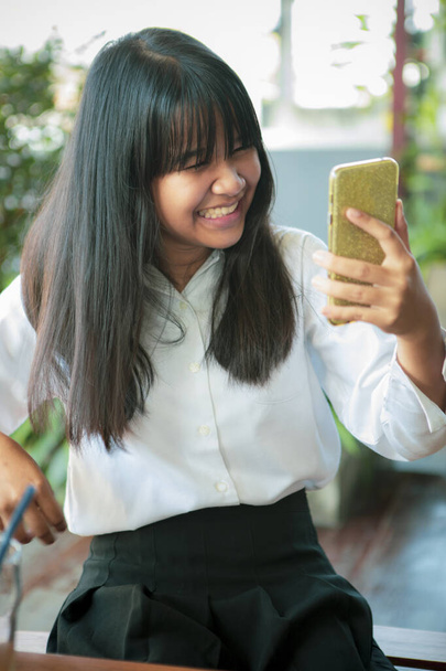 asiatischer Teenager lächelt vor Glück und blickt auf Smartphone-Bildschirm - Foto, Bild