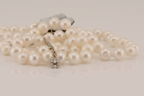 Un diamant design fleur et pendentif en or blanc niché devant des perles lustrées, isolé sur un fond blanc
 - Photo, image