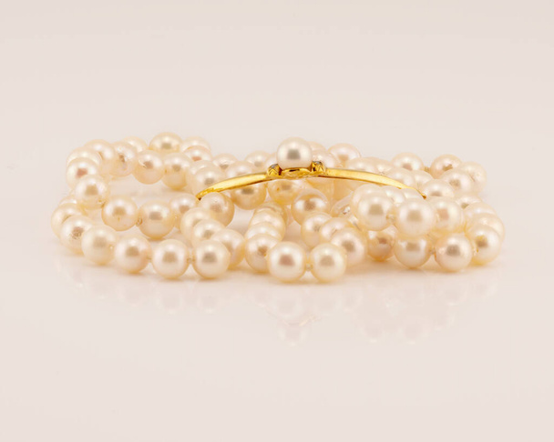 A string of lustrously glowing natural pearls designed as a necklace with a yellow gold bar center feature adorned with a pearl, isolated on a white background - Photo, Image