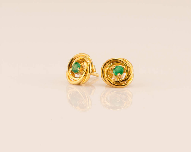 A pair of modern emerald and gold earrings designed in a swirling circular shape with the green stone in the center, isolated on a white background - Photo, Image