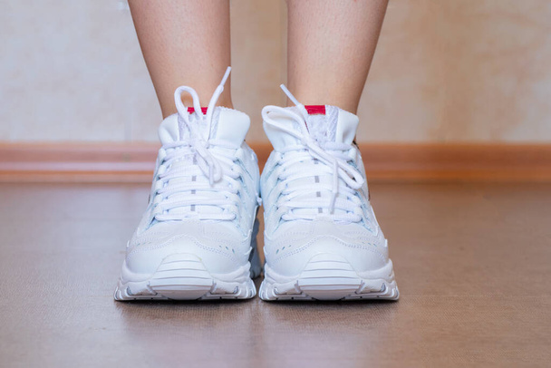 άσπρα αθλητικά παπούτσια μέσα σε ένα κορίτσι που στέκεται στο πάτωμα - Φωτογραφία, εικόνα
