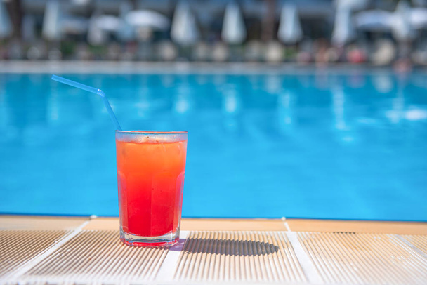 Fresh alcoholic red cocktail sex on beach with ice in glass on edge of pool in summer weather against background washed up pool and recreation area. Concept good holiday and travel, place for text. - Foto, imagen