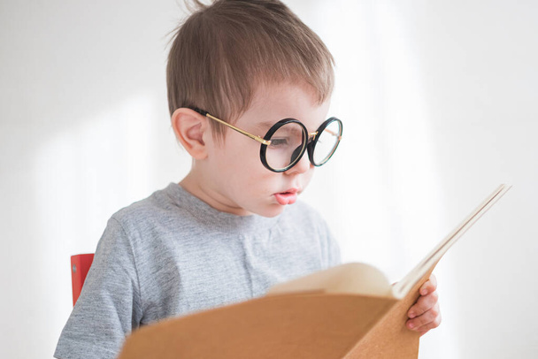 Cute toddler boy reading a book in glasses. Smart preschooler. Back to school concept - Foto, imagen