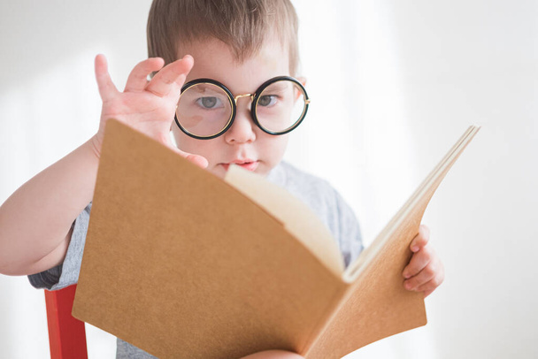 Χαριτωμένο αγοράκι που διαβάζει ένα βιβλίο με γυαλιά. Έξυπνο νηπιαγωγείο. Επιστροφή στο σχολείο έννοια - Φωτογραφία, εικόνα
