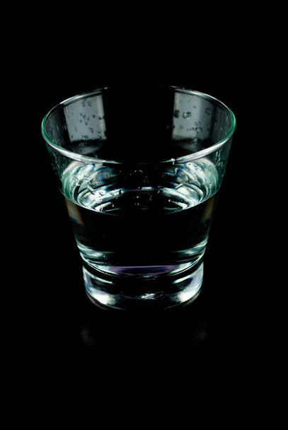 lege glazen voor whiskey op een reflecterend oppervlak op zwarte achtergrond - Foto, afbeelding