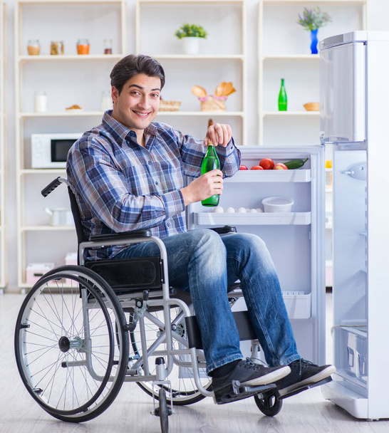Νεαρός ανάπηρος τραυματίας ανοίγει την πόρτα του ψυγείου - Φωτογραφία, εικόνα