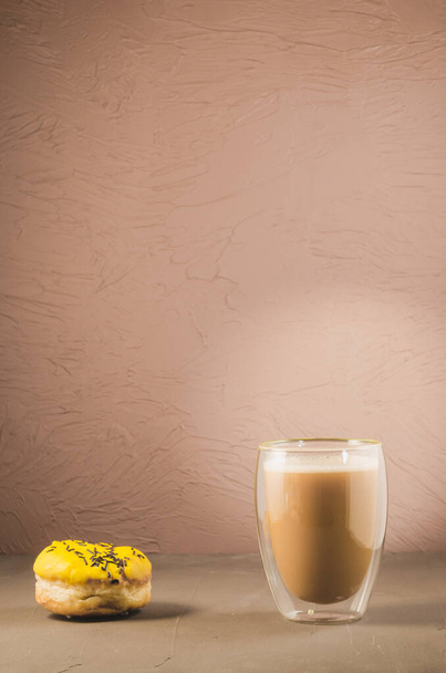 donut in yellow glaze and a cappuccino glass/donut in yellow glaze and a cappuccino glass on a brown background with copy space - Photo, Image
