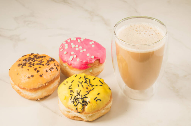 donuts in glazes and a glass of a cappuccino/donuts in glazes and a glass of a cappuccino on a white table. Selective focus - Foto, Imagem