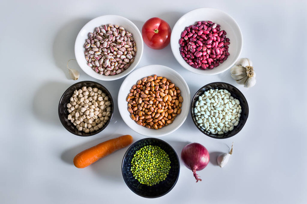 Set of products for making a recipe from legumes: phaseolus; beans; chickpeas; mung beans; tomatoes, onions, carrots, garlic and herbs. - Фото, изображение