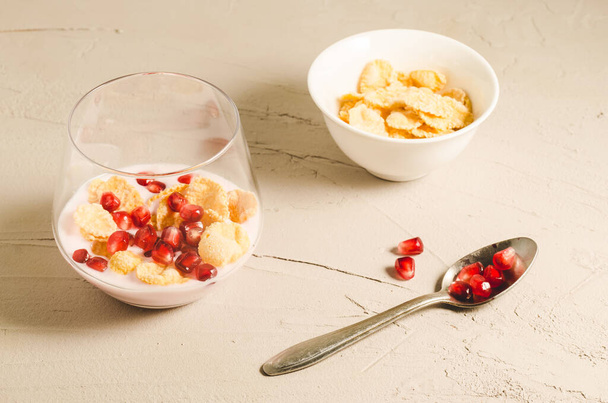 homemade yogurt with pomegranate in glass and a bowl of flakes/homemade yogurt with pomegranate in glass and a bowl of flakes on a white stone table - Fotoğraf, Görsel