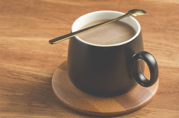black mug of a cappuccino in a wooden support, on a wooden table - Фото, зображення