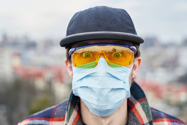 Junger Mann in Freizeitkleidung mit medizinischer Maske und Schutzbrille gegen Coronavirus und Umweltverschmutzung - Foto, Bild