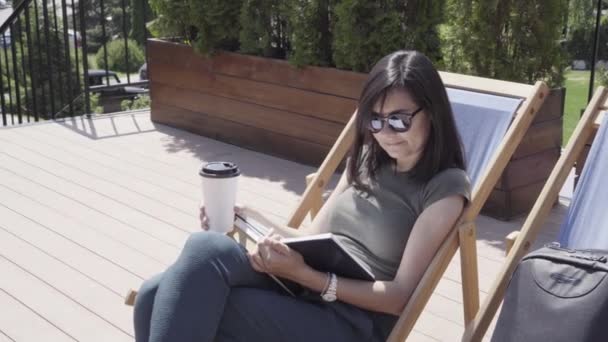 Young woman reading a book sitting on a sun lounger on a sunny day. - Video