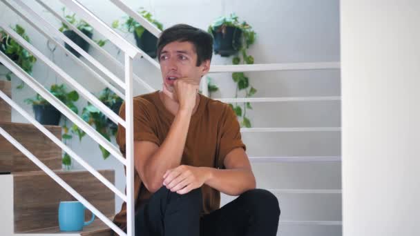 Pensive sad and depressed young man sitting alone on stairs at home: painful sad man. - Materiał filmowy, wideo