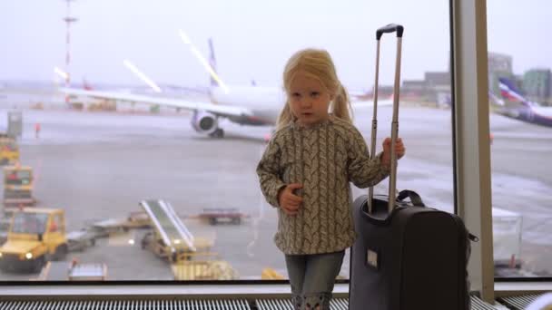 Een meisje met een koffer op het vliegveld. Kind op het vliegveld in de wachtkamer. - Video