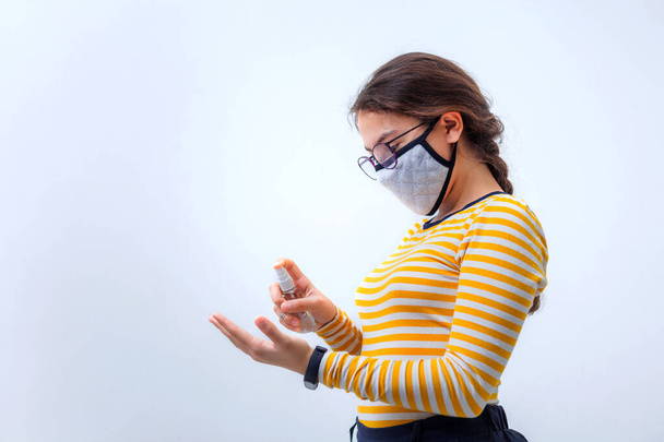 Nastolatka w masce medycznej traktuje dłonie środkiem antyseptycznym na zimnym szarym tle z przestrzenią do kopiowania. Wirus. Ostre zakażenie wirusowe dróg oddechowych. Zimna choroba. Maska ochronna. Środki ostrożności w przypadku epidemii - Zdjęcie, obraz