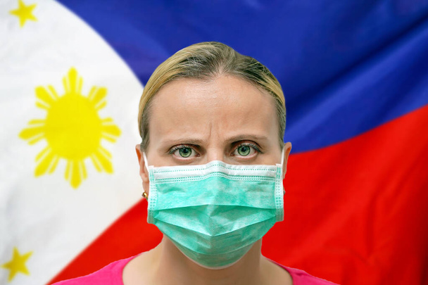 Жінка з маскою дивиться на камеру на тлі прапора Філіппін. Концепція уваги до всесвітнього поширення коронавірусу по всьому світу. Коронавірус у Філіппінах. - Фото, зображення