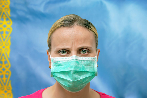 仮面の女性の顔のフラグカザフスタンの背景には、カメラを見て。世界中のコロナウイルスに注目するというコンセプト。コロナウイルス、カザフスタンのウイルス. - 写真・画像