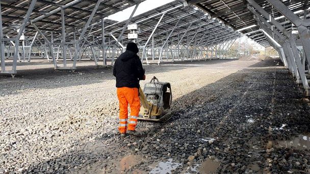 Um funcionário usando uma máquina vibratória comprime os escombros no futuro Estacionamento sob os painéis solares
. - Foto, Imagem