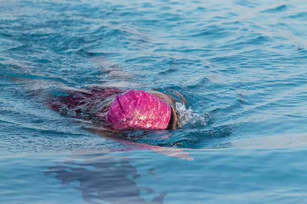Zblízka žena plave směrem ke kameře v modrém venkovním bazénu. - Fotografie, Obrázek