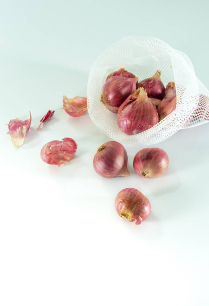 Red onions in mesh bag and some on floor isolated on white background - Photo, Image