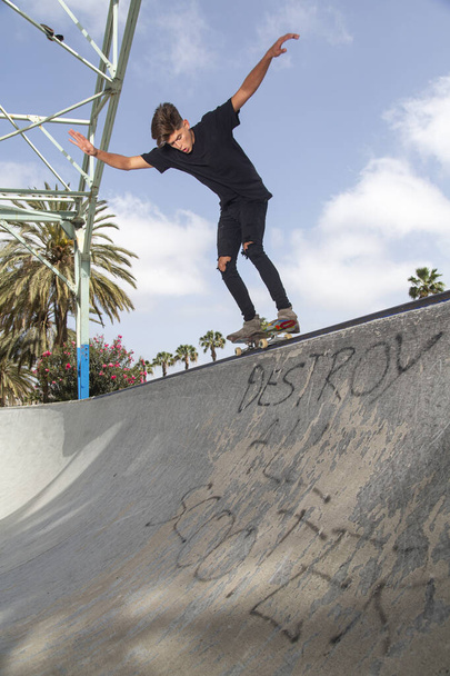 Jonge skateboarder die trucs uithaalt in een park, met straatachtergrond en blauwe lucht. - Foto, afbeelding