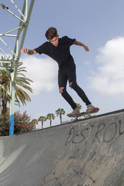 Jonge skateboarder die trucs uithaalt in een park, met straatachtergrond en blauwe lucht. - Foto, afbeelding