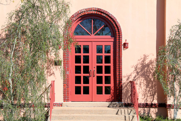 ретро-здание с ярко-красным арочным входом и ступенями
 - Фото, изображение