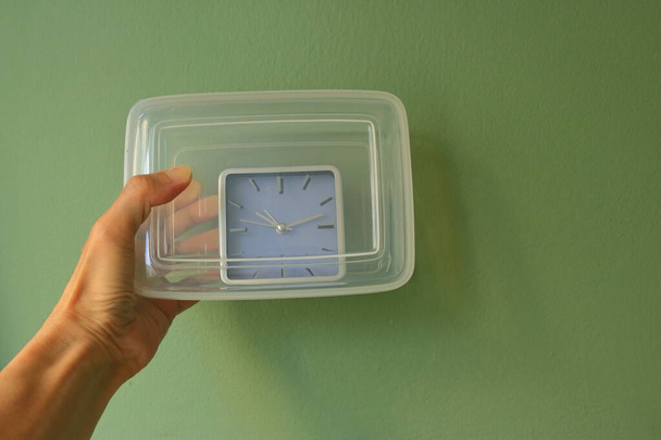 Hand hält eine geschlossene Kunststoffbox mit analoger Uhr darin. Zeitersparnis, haben Sie ein gutes Zeitkonzept Metapher  - Foto, Bild