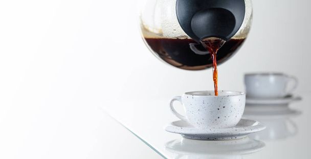 Café negro en una taza de cerámica sobre una mesa de vidrio. El café se vierte de la cafetera en una taza. Copiar espacio. - Foto, imagen