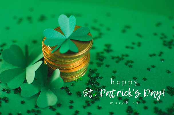 St. Patricks Day message with close up stack of chocolate coins with green four-leafed paper shamrocks on green blurred background with small stars. Greeting card with text. Lucky concept - Photo, Image