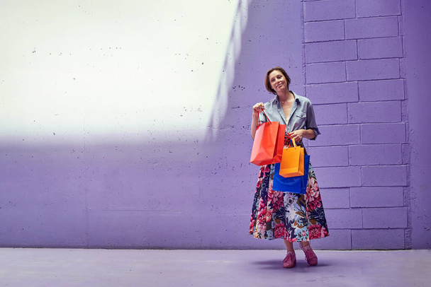 Young beautiful girl with packages shopping in hands. A girl in a long bright skirt and pale pink top is walking from the store. - Foto, Bild