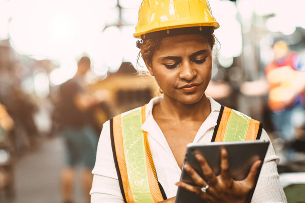 Amerikai női dolgozó nehézipari karbantartó mérnök boldog dolgozó visel biztonsági egyenruhát és sisak segítségével tabletta számítógép ellenőrző gép a gyárban. - Fotó, kép