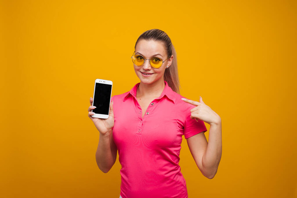 Bright and positive young woman with smartphone on yellow background. The girl uses a smartphone - Фото, изображение