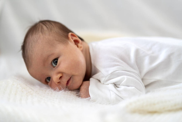 A 3 week old Caucasian baby girl smiles as he lays on a fluffy down duvet comforter on a bed - Фото, зображення