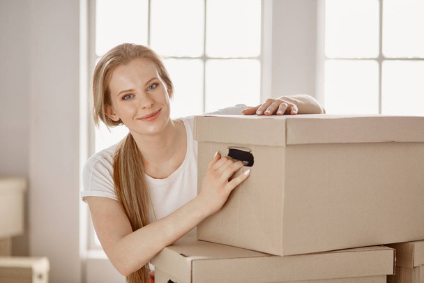 Μια όμορφη ανύπαντρη γυναίκα ξεπακετάρει κουτιά και μετακομίζει σε νέο σπίτι. - Φωτογραφία, εικόνα