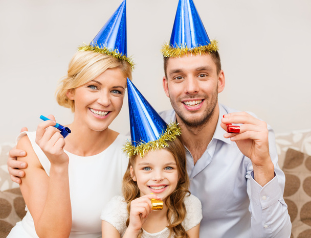 Smiling family in blue hats blowing favor horns - Foto, Bild